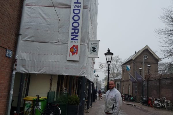 Ingepakte steiger op de hoek van gevel Springhavertheater in Utrecht. Schilder poseert onder logo Joh. van Doorn De Bilt BV.